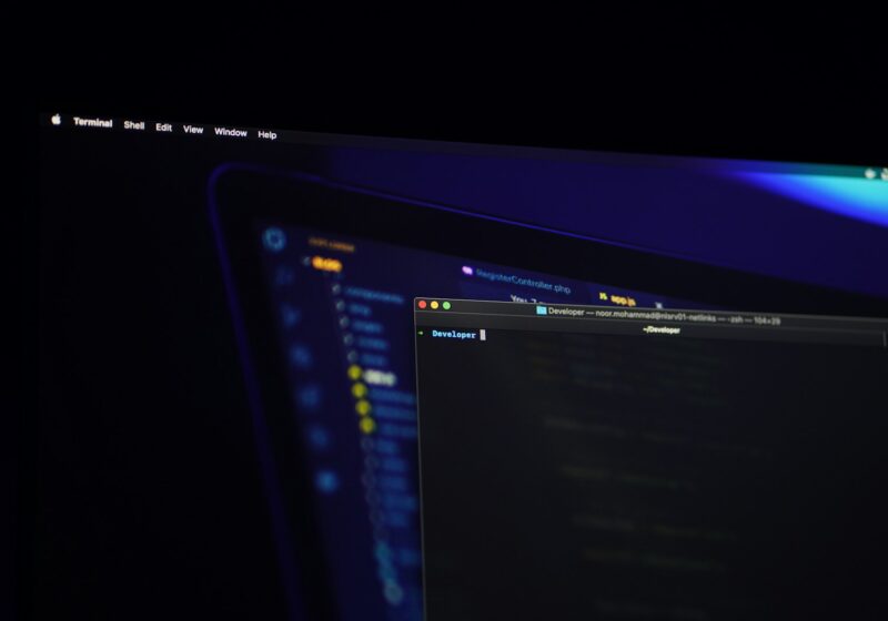 Multiple computer screens displaying software code in a dark developer workspace
