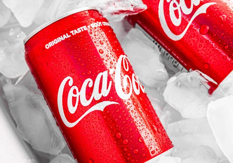 Coca-Cola bottles and cans on ice, showing the brand's distinctive red-and-white visual identity.