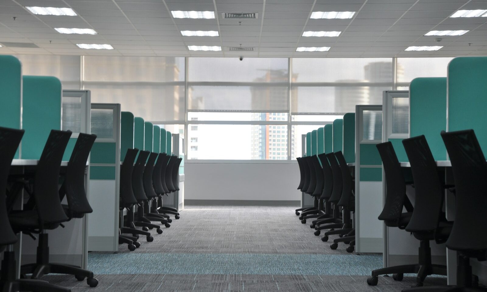 Rows of empty office cubicles and black rolling chairs in a corporate workspace.