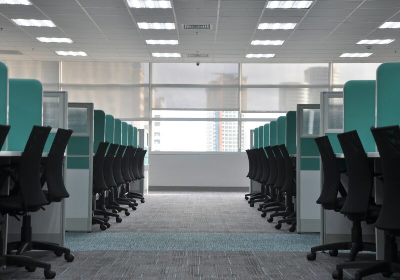Rows of empty office cubicles and black rolling chairs in a corporate workspace.