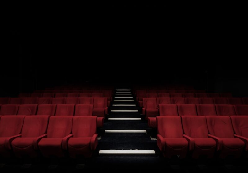 Rows of empty red cinema seats facing a movie screen, illustrating changes in theatrical attendance and the box office.