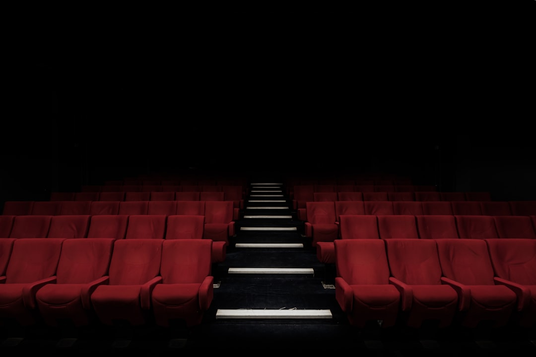 Rows of empty red cinema seats facing a movie screen, illustrating changes in theatrical attendance and the box office.