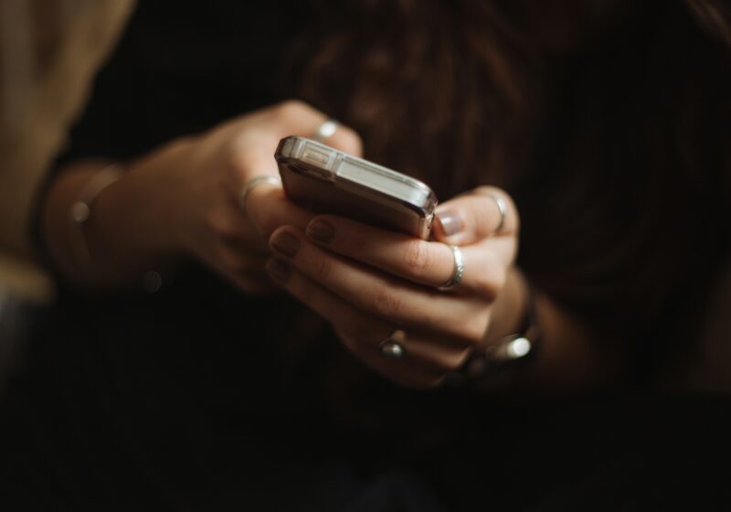 Illustrative image of a person using a smartphone beside a laptop