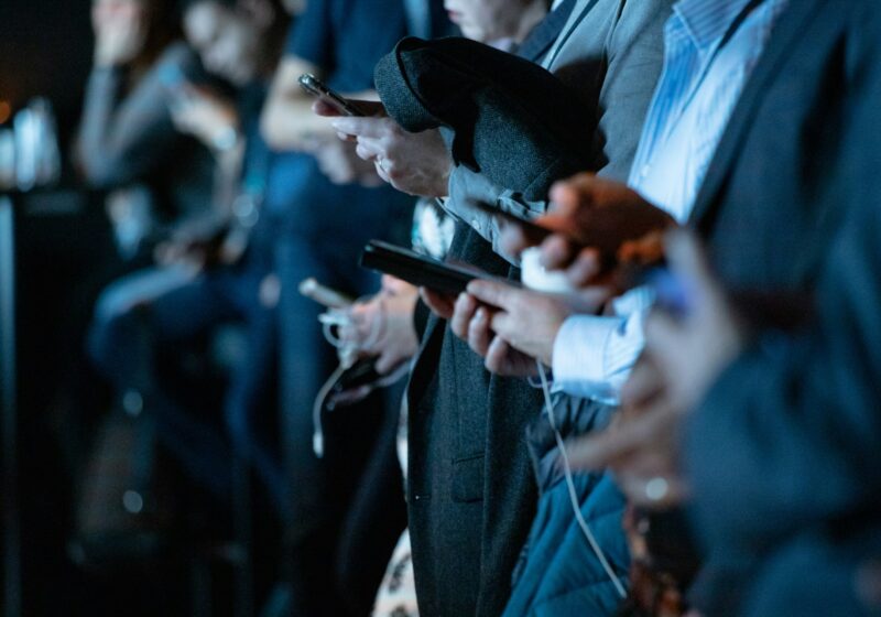 People standing together while looking at smartphones
