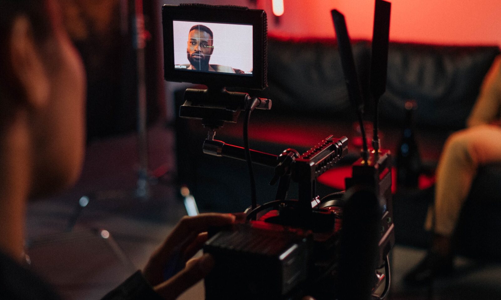 A camera operator works on a production set under red studio lighting.