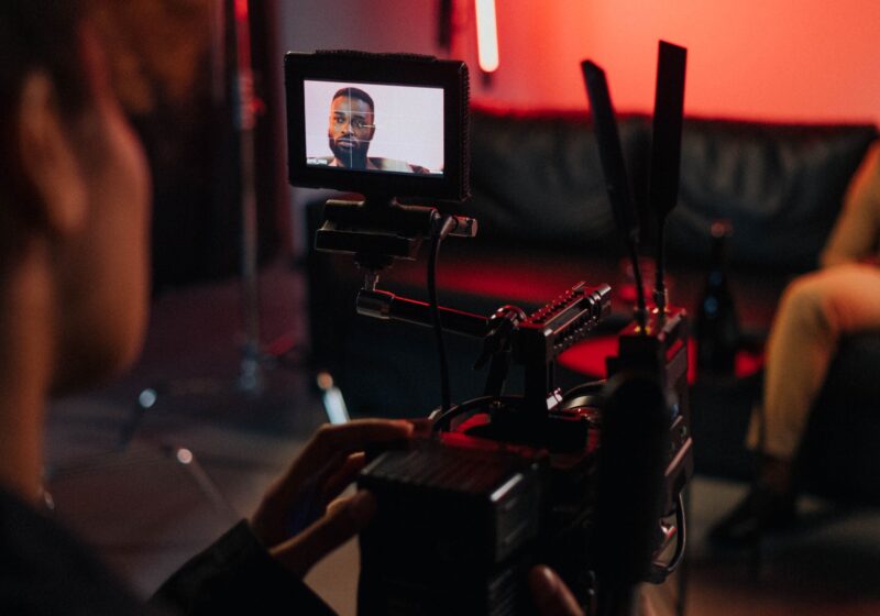 A camera operator works on a production set under red studio lighting.