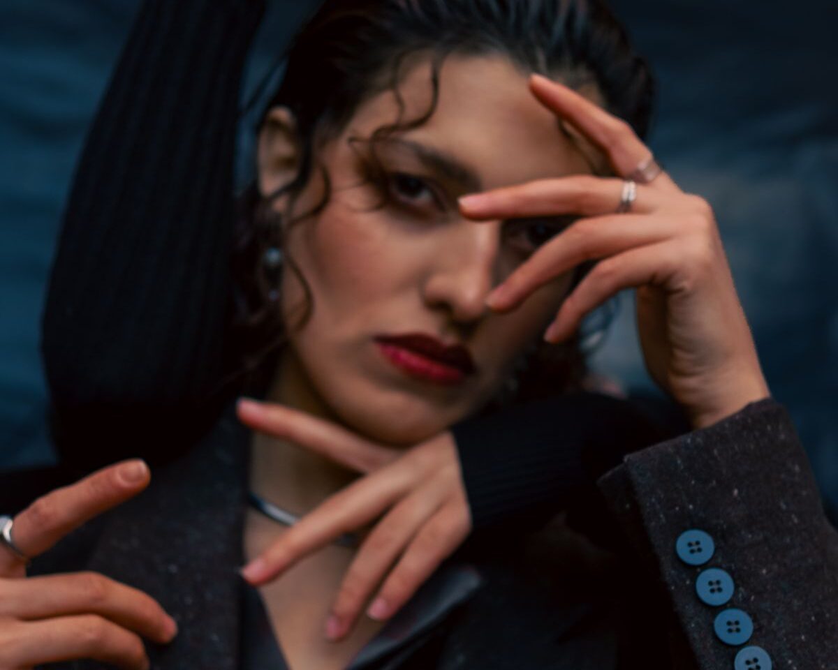 An editorial portrait with dramatic hand gestures and dark styling.