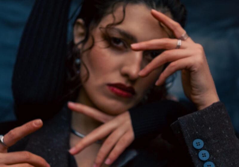 An editorial portrait with dramatic hand gestures and dark styling.