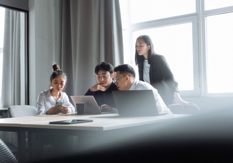 Four colleagues reviewing work together around laptops.