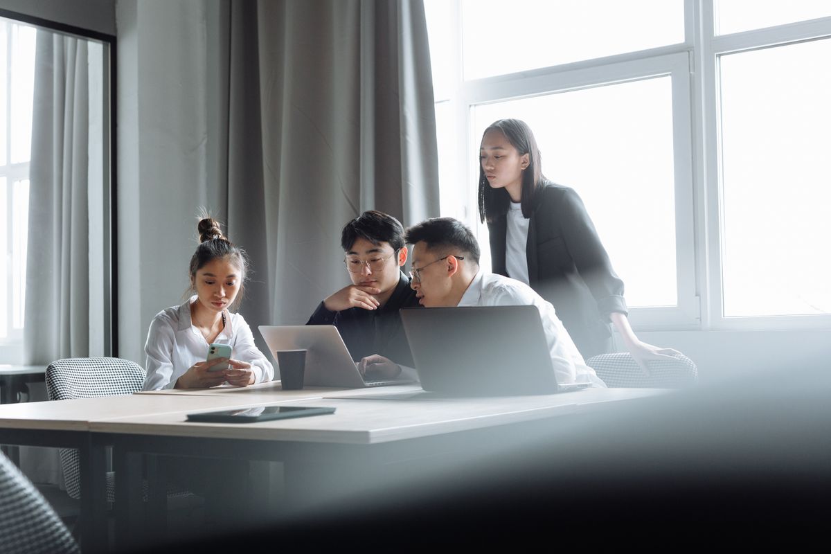 Four colleagues reviewing work together around laptops.