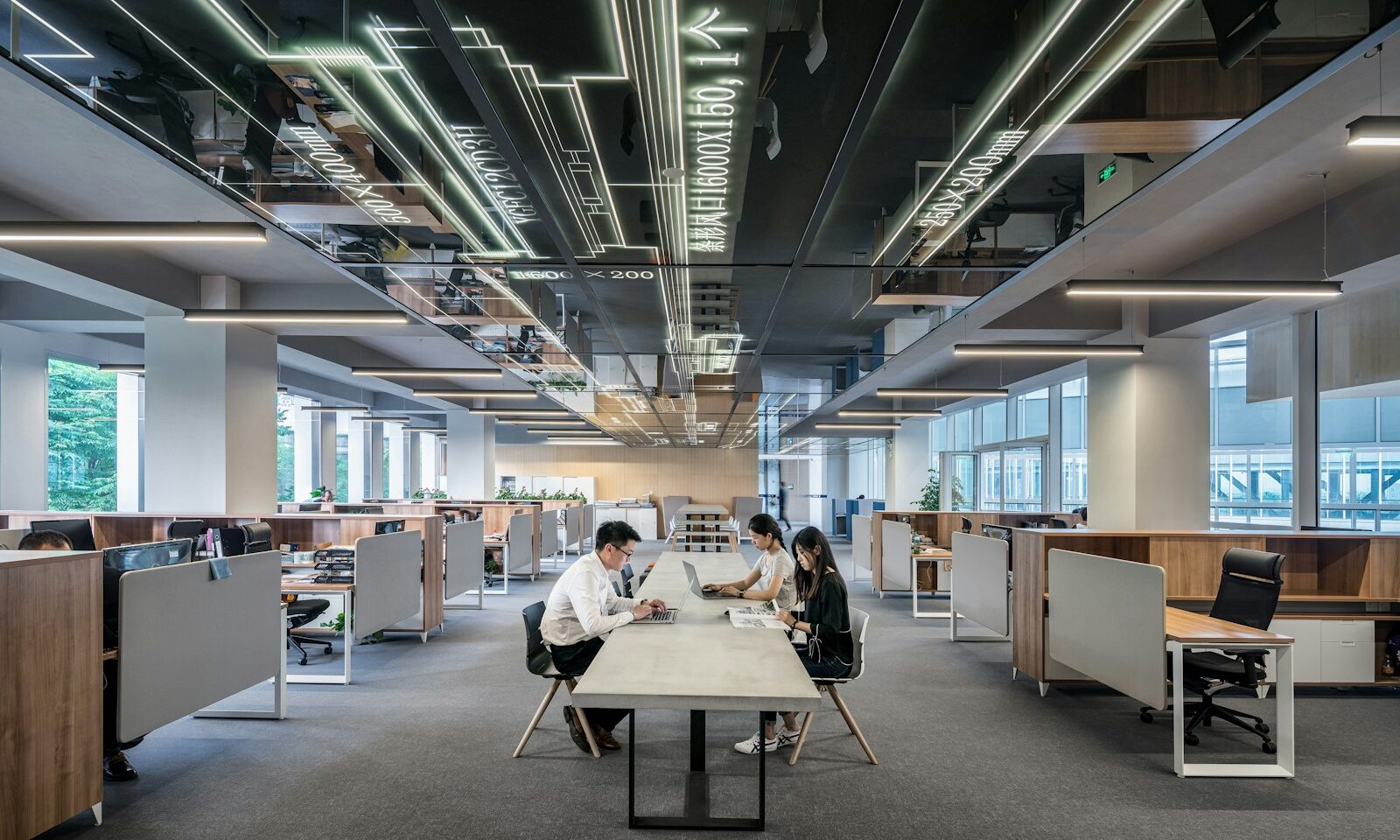 Three people working at laptops around a shared table in a modern open-plan office.
