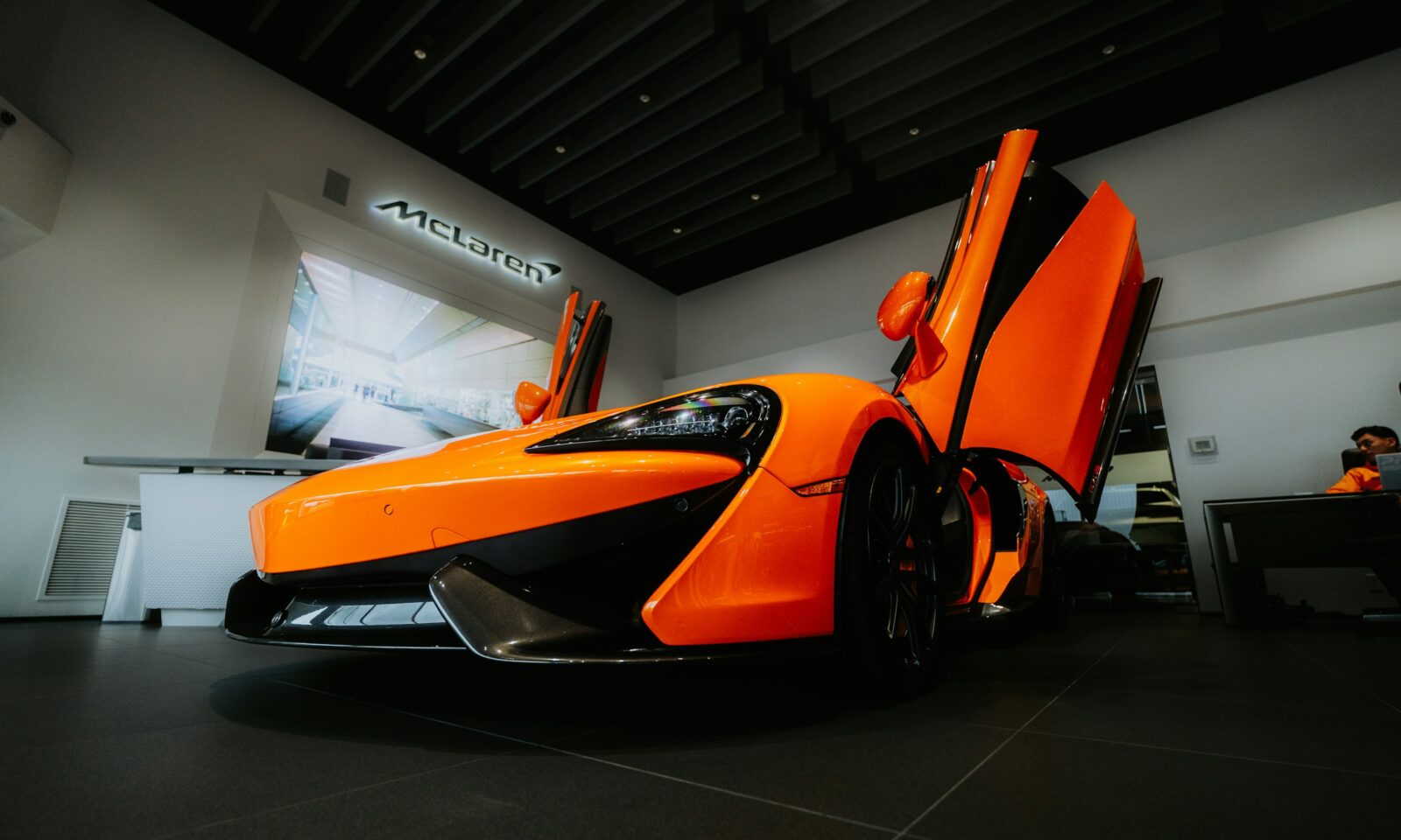 Orange McLaren sports car displayed in a showroom with its doors raised; archival illustrative photograph, not the new 2026 identity.