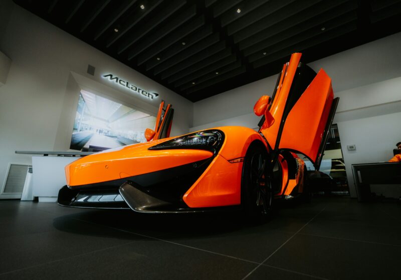 Orange McLaren sports car displayed in a showroom with its doors raised; archival illustrative photograph, not the new 2026 identity.