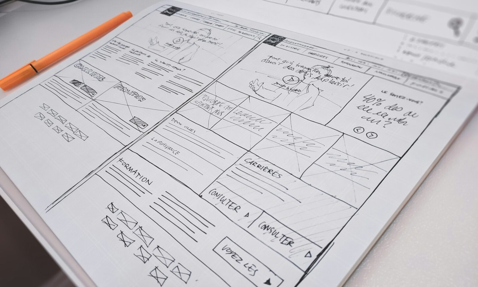 Hand-drawn website wireframe and orange pen on a desk
