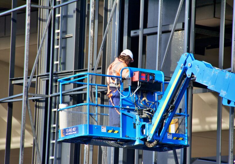 Construction worker operating a lift beside the frame of a building