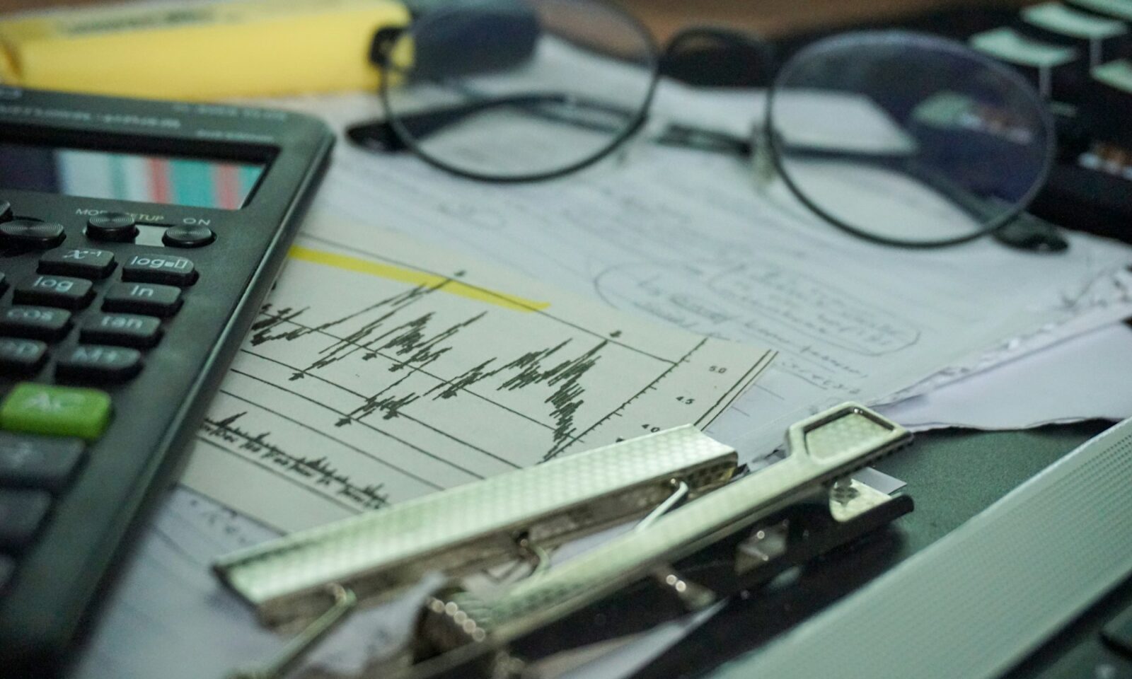 Calculator, eyeglasses and financial charts arranged on a desk.