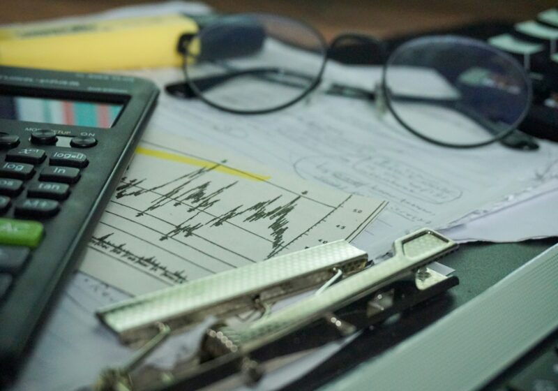 Calculator, eyeglasses and financial charts arranged on a desk.