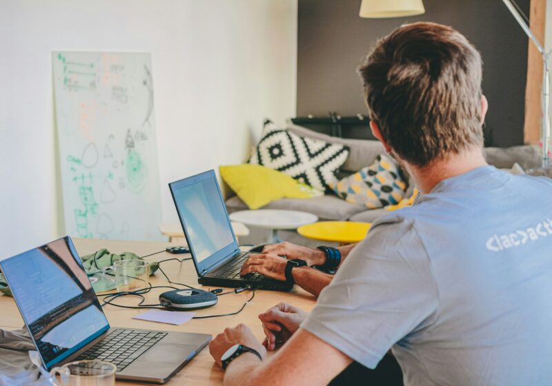 Professional working across two laptop computers, illustrating enterprise AI management
