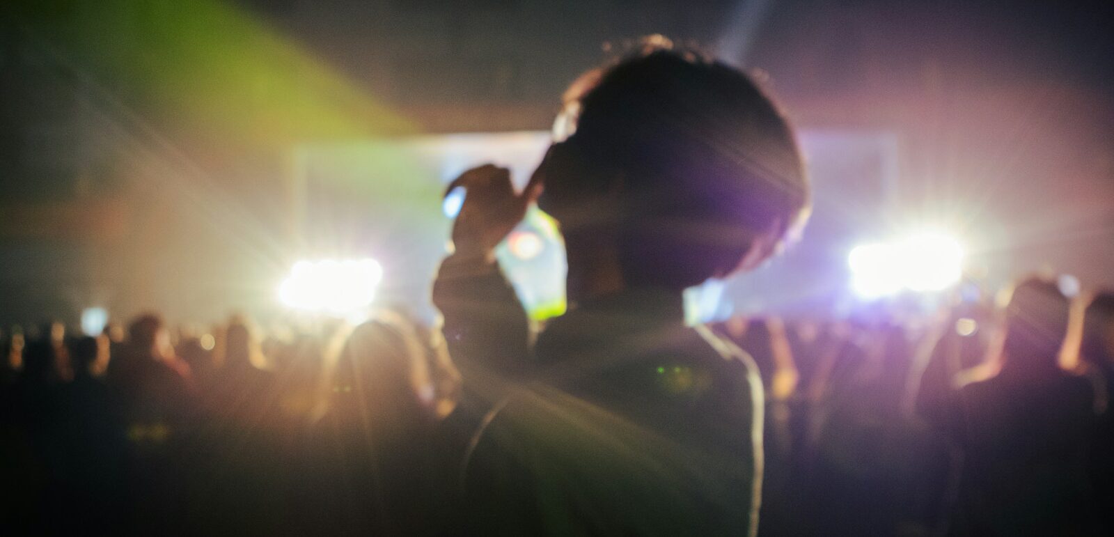 Silhouetted concertgoer facing bright stage lights at a live music performance