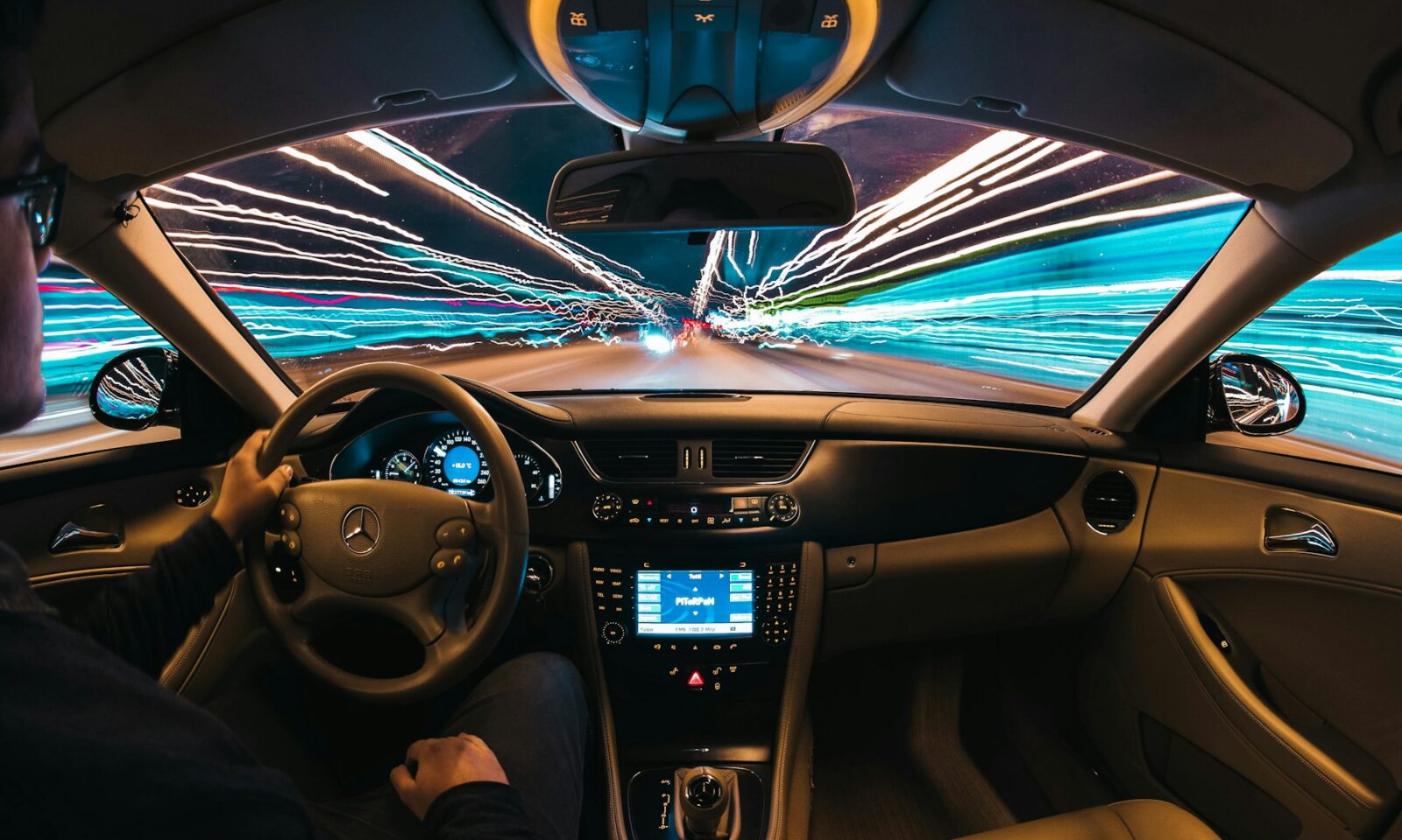 Driver operating a conventional vehicle at night, illustrating the manual controls absent from purpose-built robotaxis.