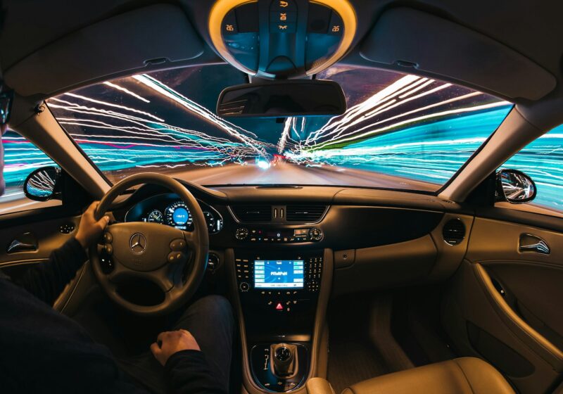 Driver operating a conventional vehicle at night, illustrating the manual controls absent from purpose-built robotaxis.