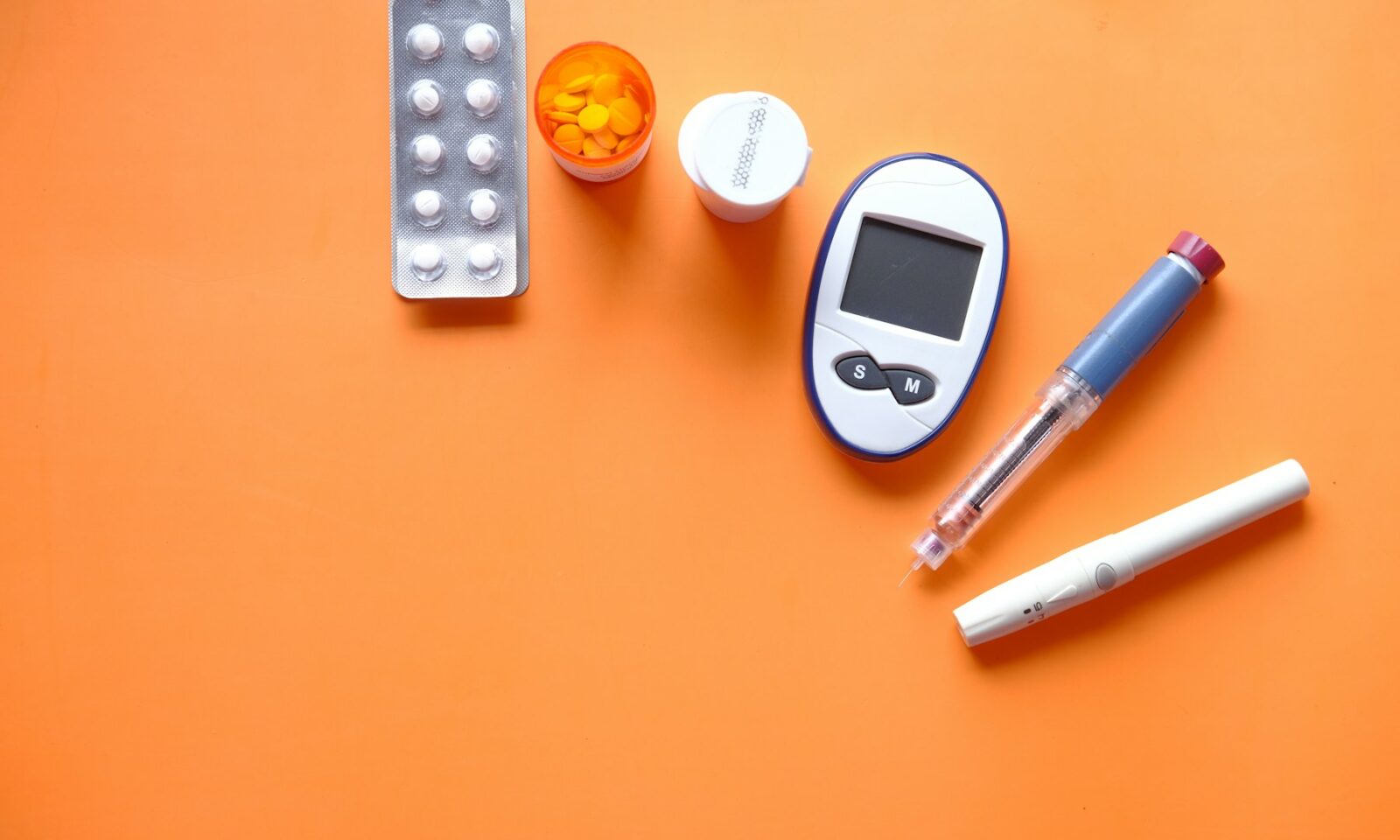 Insulin pen, glucose meter and medication arranged on an orange surface