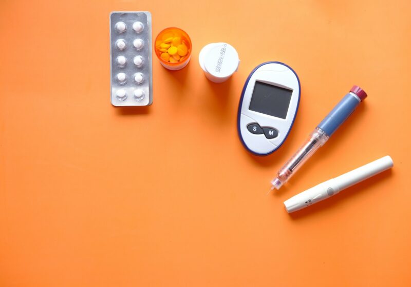Insulin pen, glucose meter and medication arranged on an orange surface