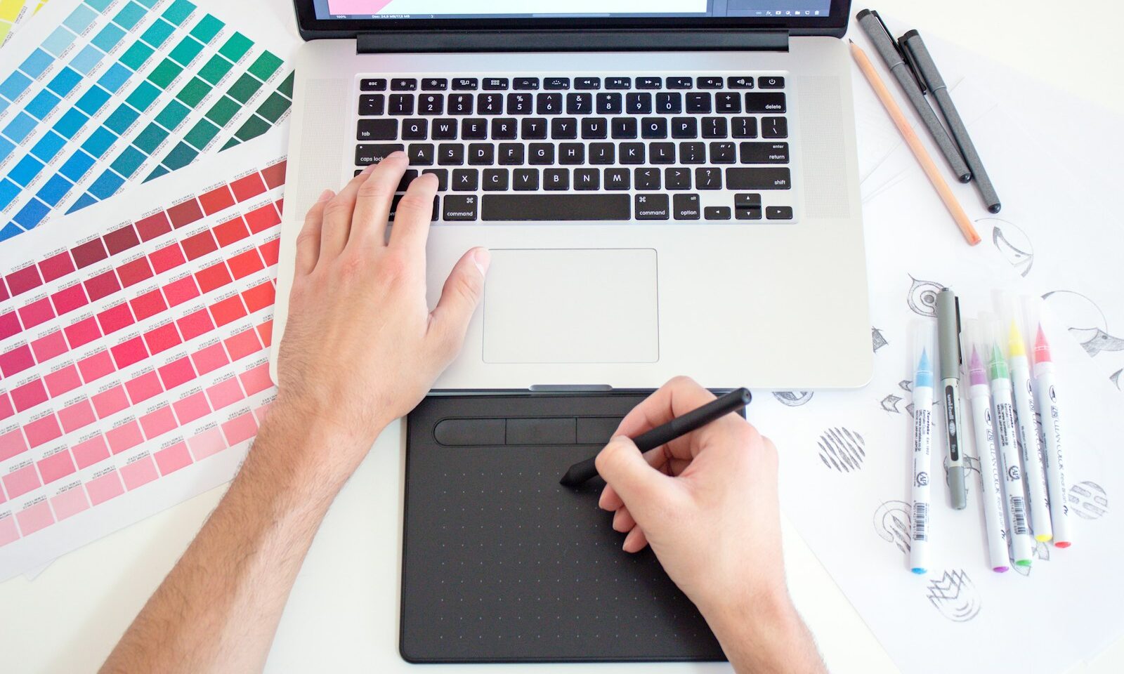 Designer using a tablet and laptop beside color charts