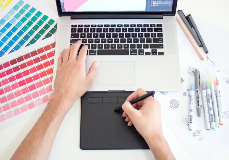 Designer using a tablet and laptop beside color charts