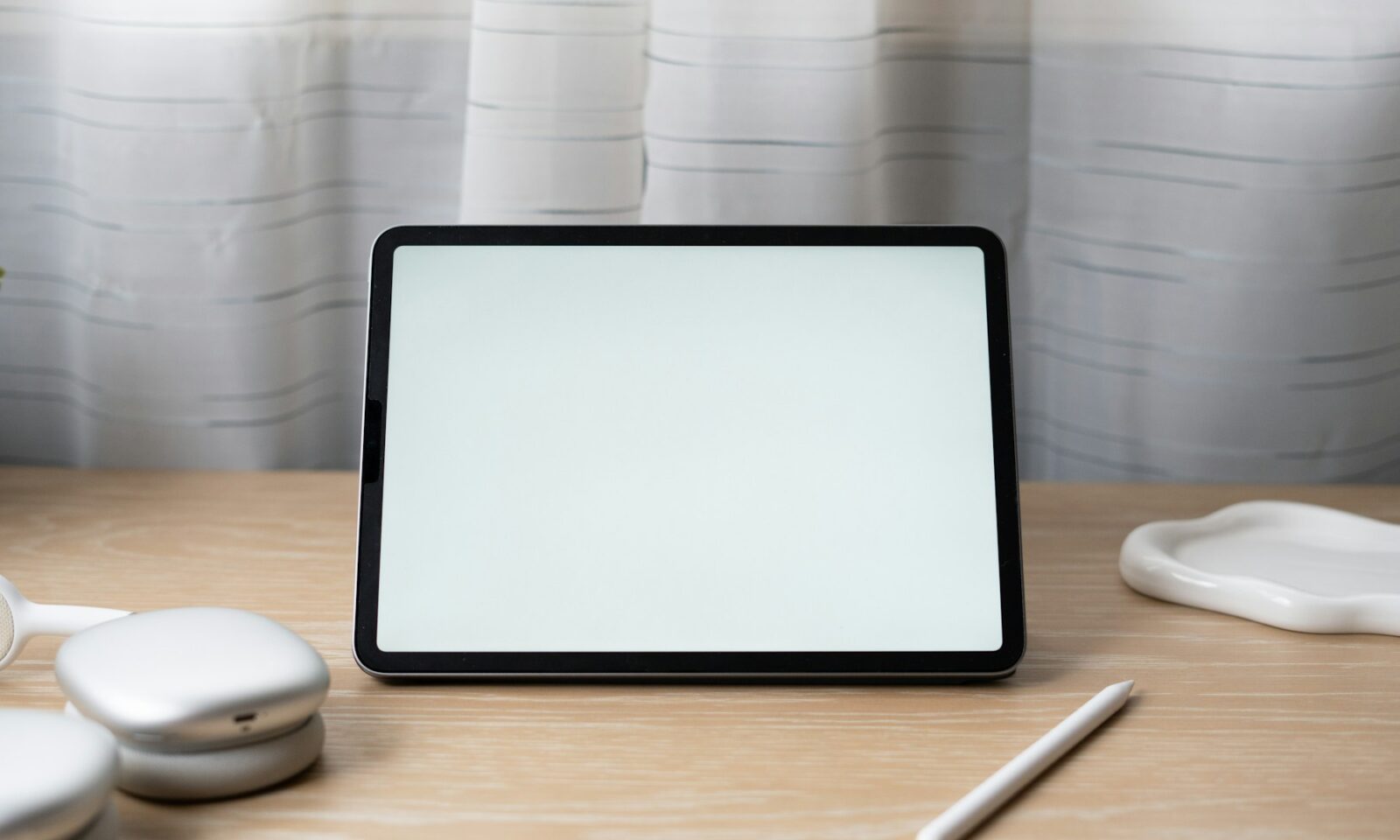 An older iPad Pro with a blank screen on a wooden desk beside headphones and a stylus; not the new iPad mini