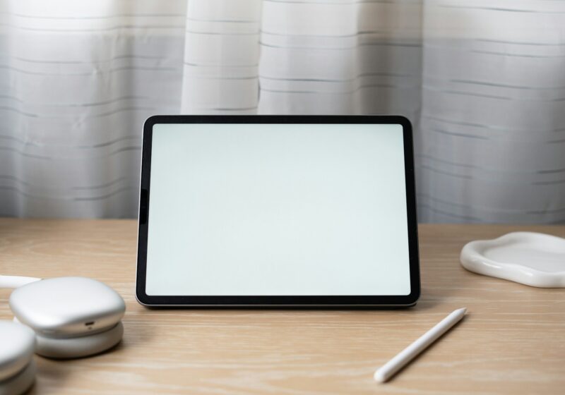 An older iPad Pro with a blank screen on a wooden desk beside headphones and a stylus; not the new iPad mini