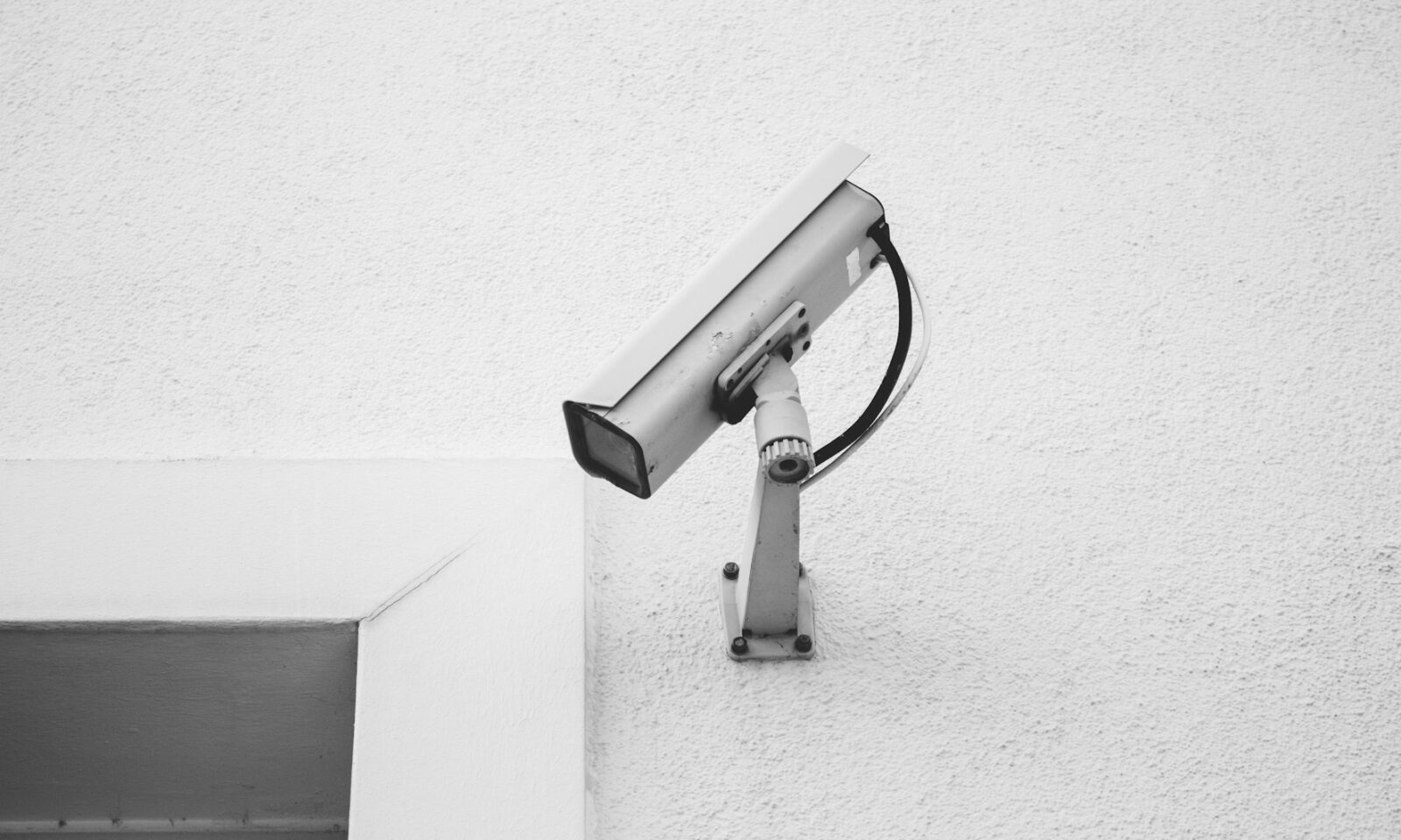 A surveillance camera mounted on a textured white wall