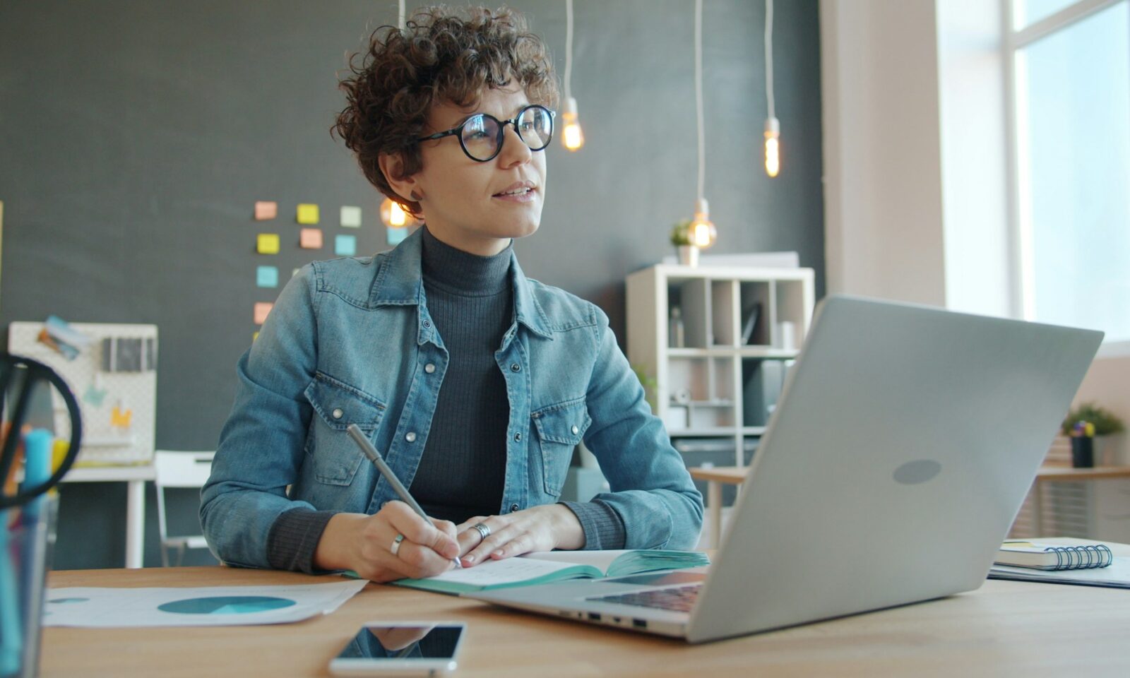 Woman working alone at a desk with a laptop and notebook