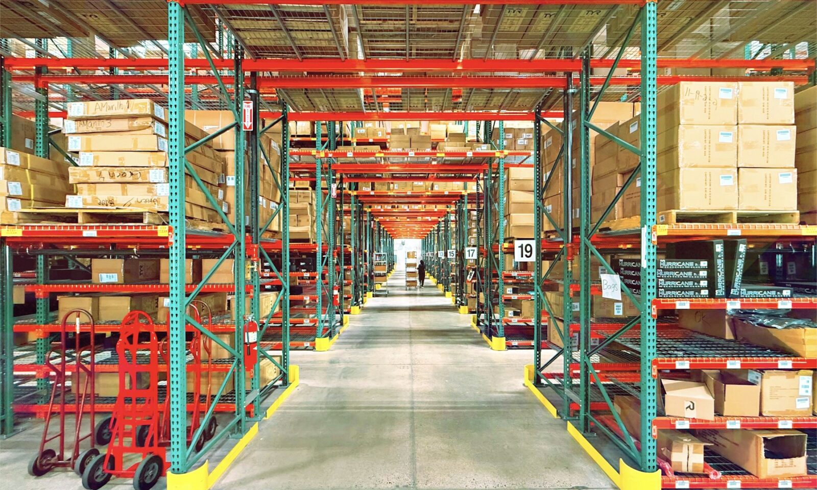 A warehouse aisle with red and green shelving, boxes and hand trucks in Huntington Beach, California; not a GXO facility