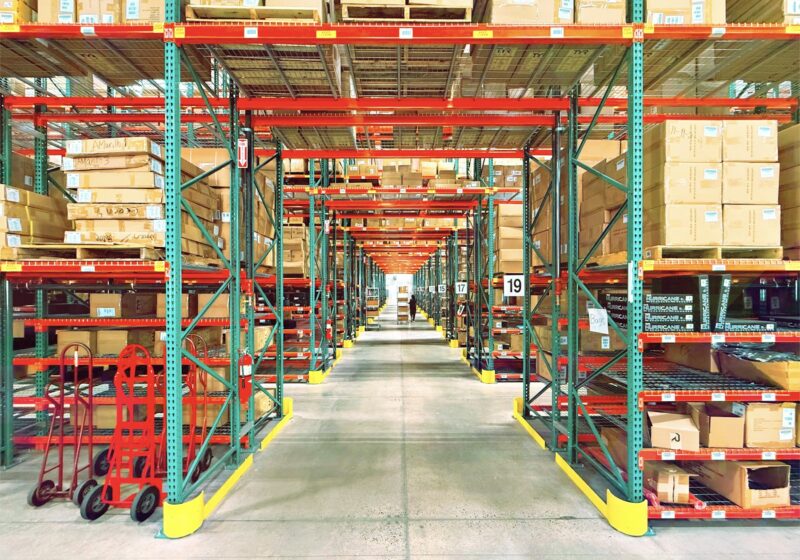 A warehouse aisle with red and green shelving, boxes and hand trucks in Huntington Beach, California; not a GXO facility